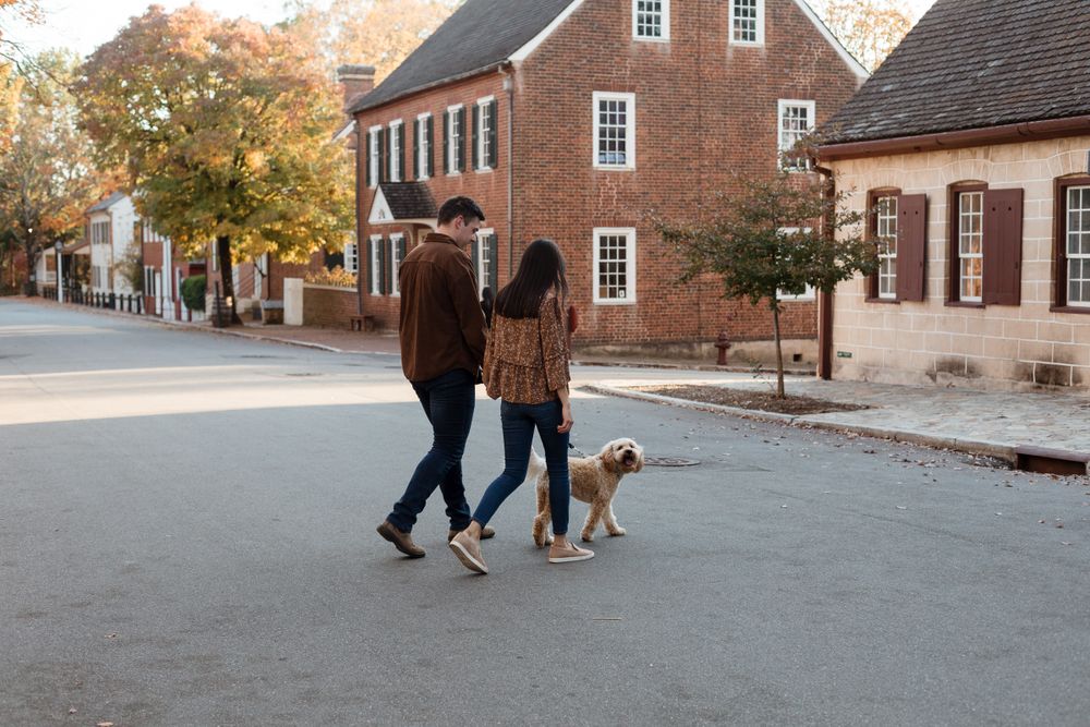 Couple strolls with their dog along historic brick buildings in autumn setting.