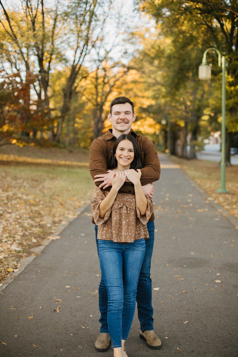 A couple poses playfully on a path surrounded by fall foliage.