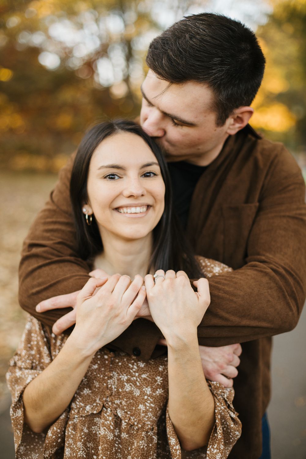 A couple embraces while wearing brown and floral outfits against a backdrop of fall colors.