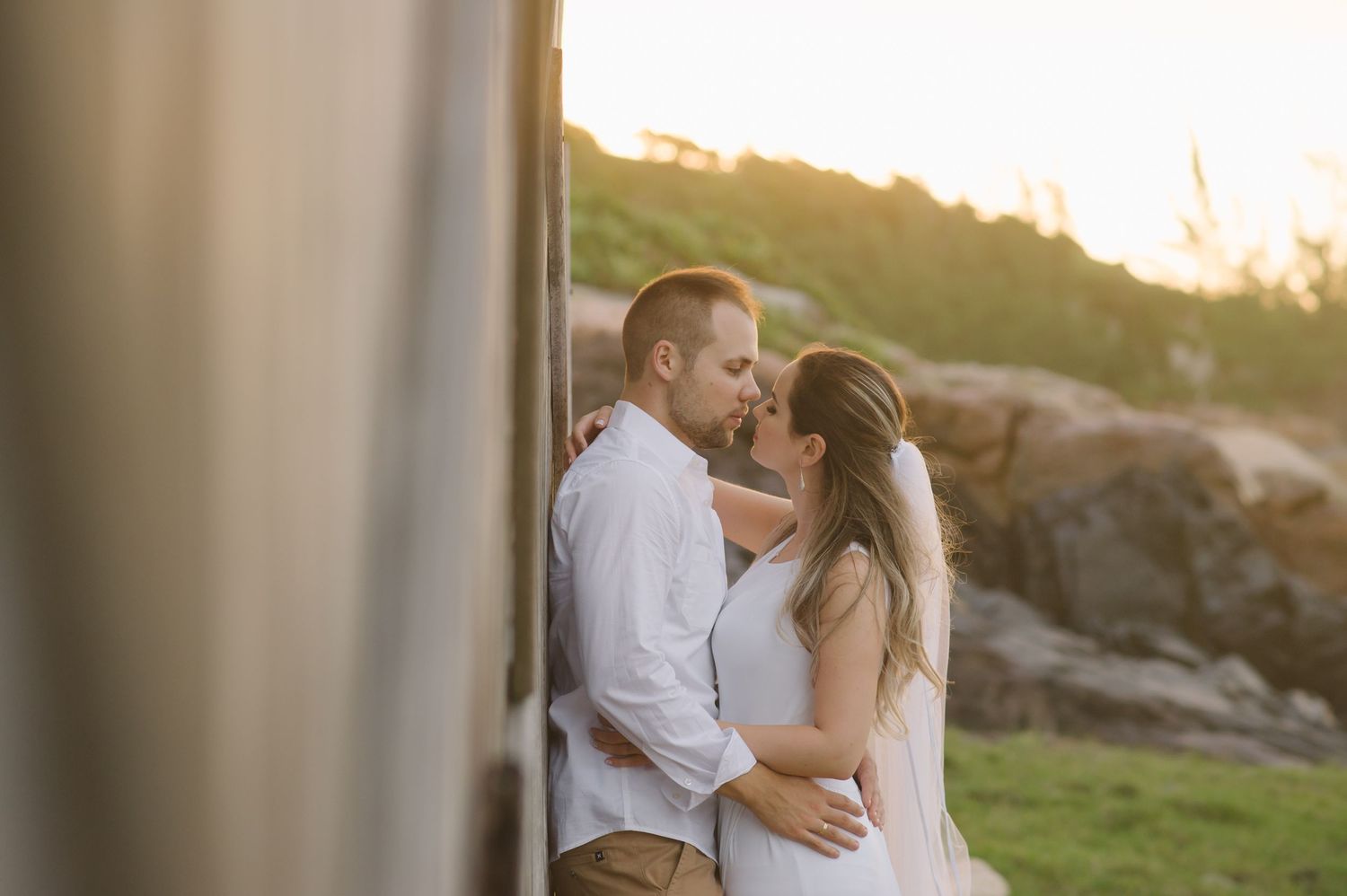 A romantic sunset wedding portrait captured against a rocky coastal landscape.
