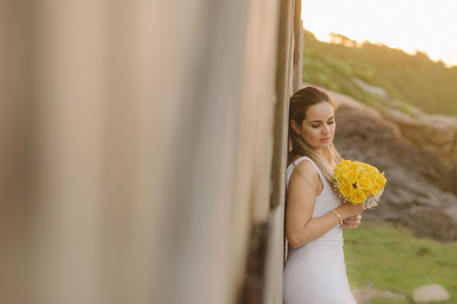 A bride holds a vibrant yellow bouquet while posing beside a rustic wall.