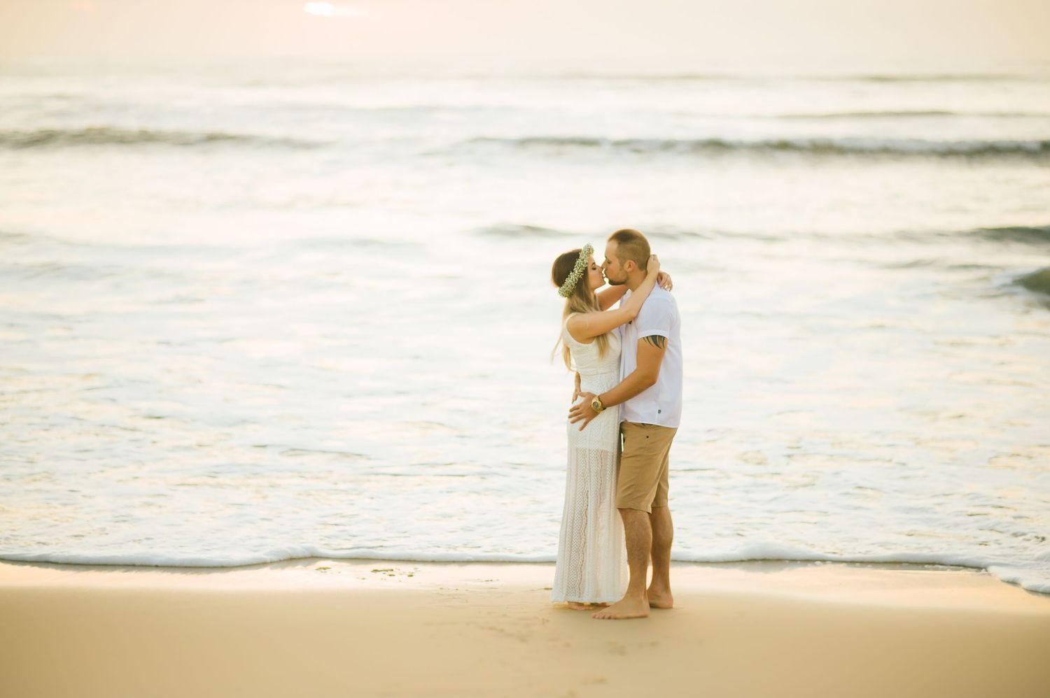 A tender moment shared on a sandy beach at sunset with waves in the background.