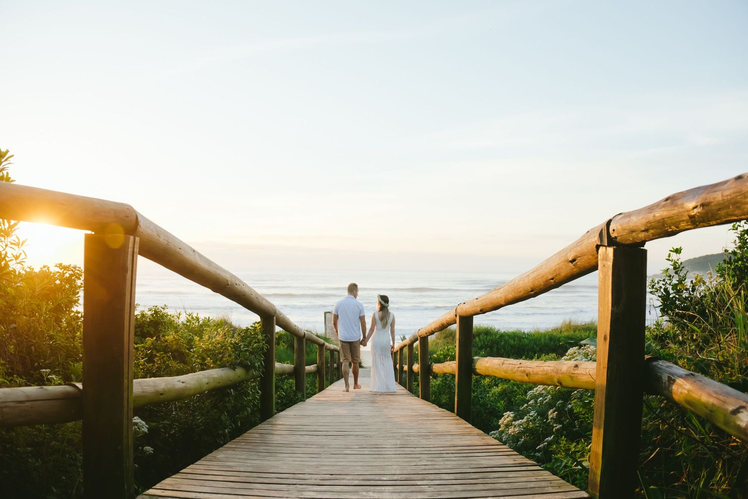 A wooden boardwalk leads to the ocean during golden hour.