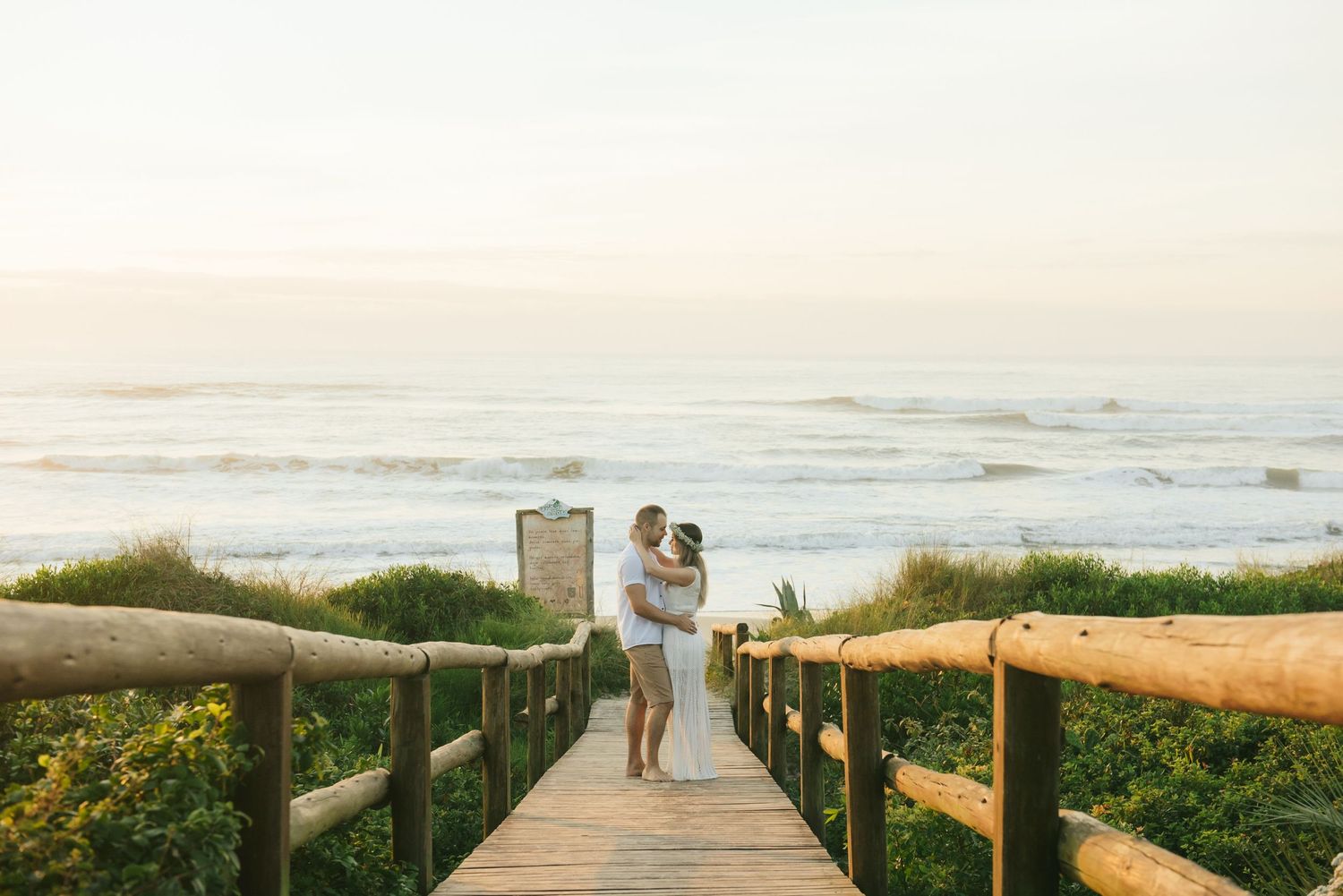 A wooden boardwalk path leads to the ocean during sunset.