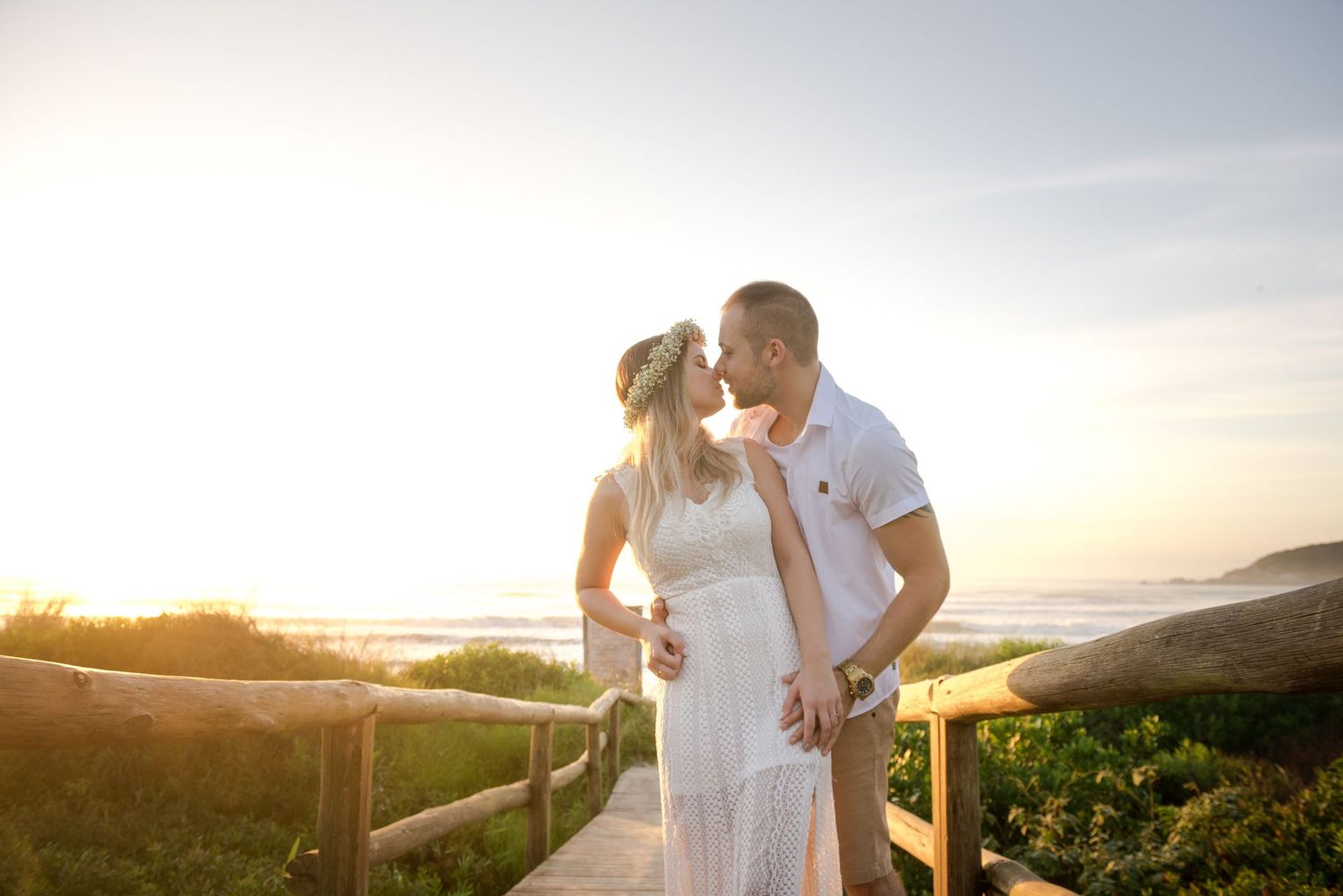 A romantic couple embraces on a scenic overlook at sunset with coastal views in the background.