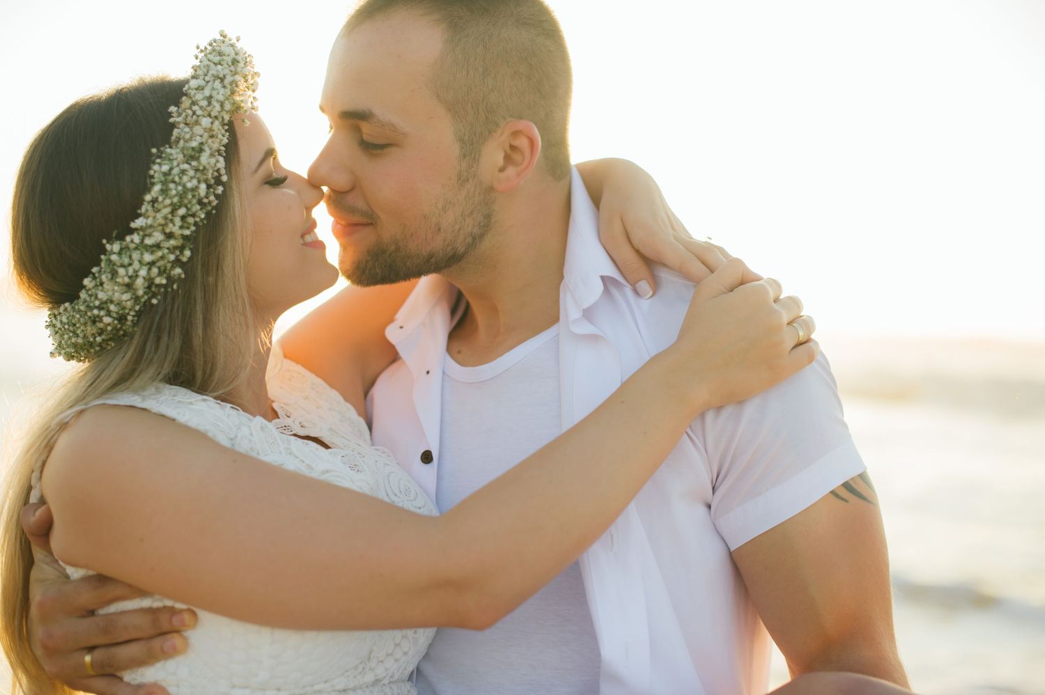 A couple shares an intimate moment at golden hour while wearing white summer attire.