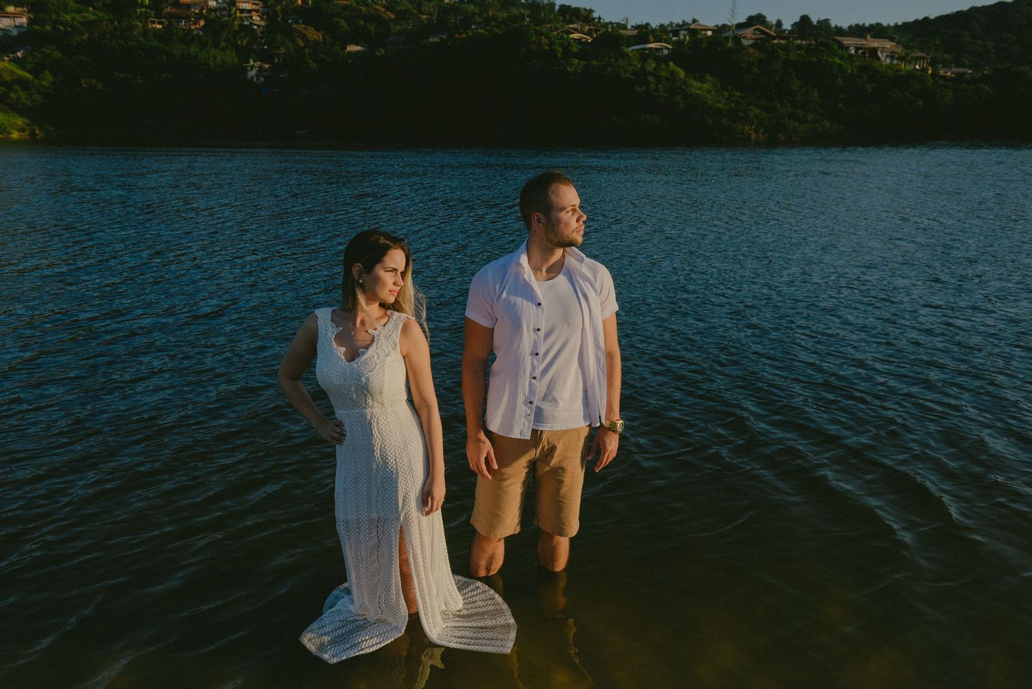 A couple poses together while standing in a lake with mountains in the background.
