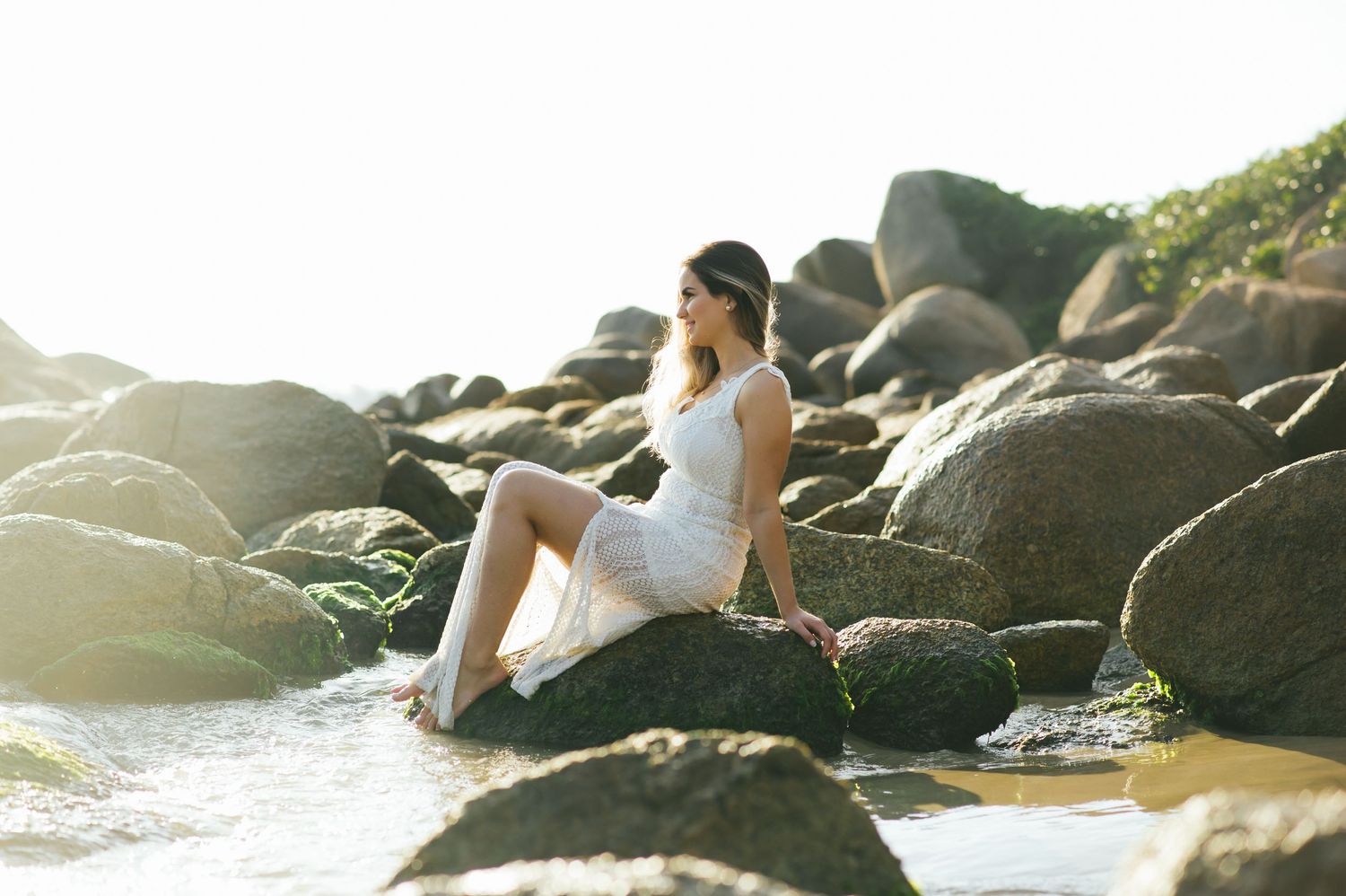 Figure sits on coastal rocks during golden hour with sunlight streaming through.