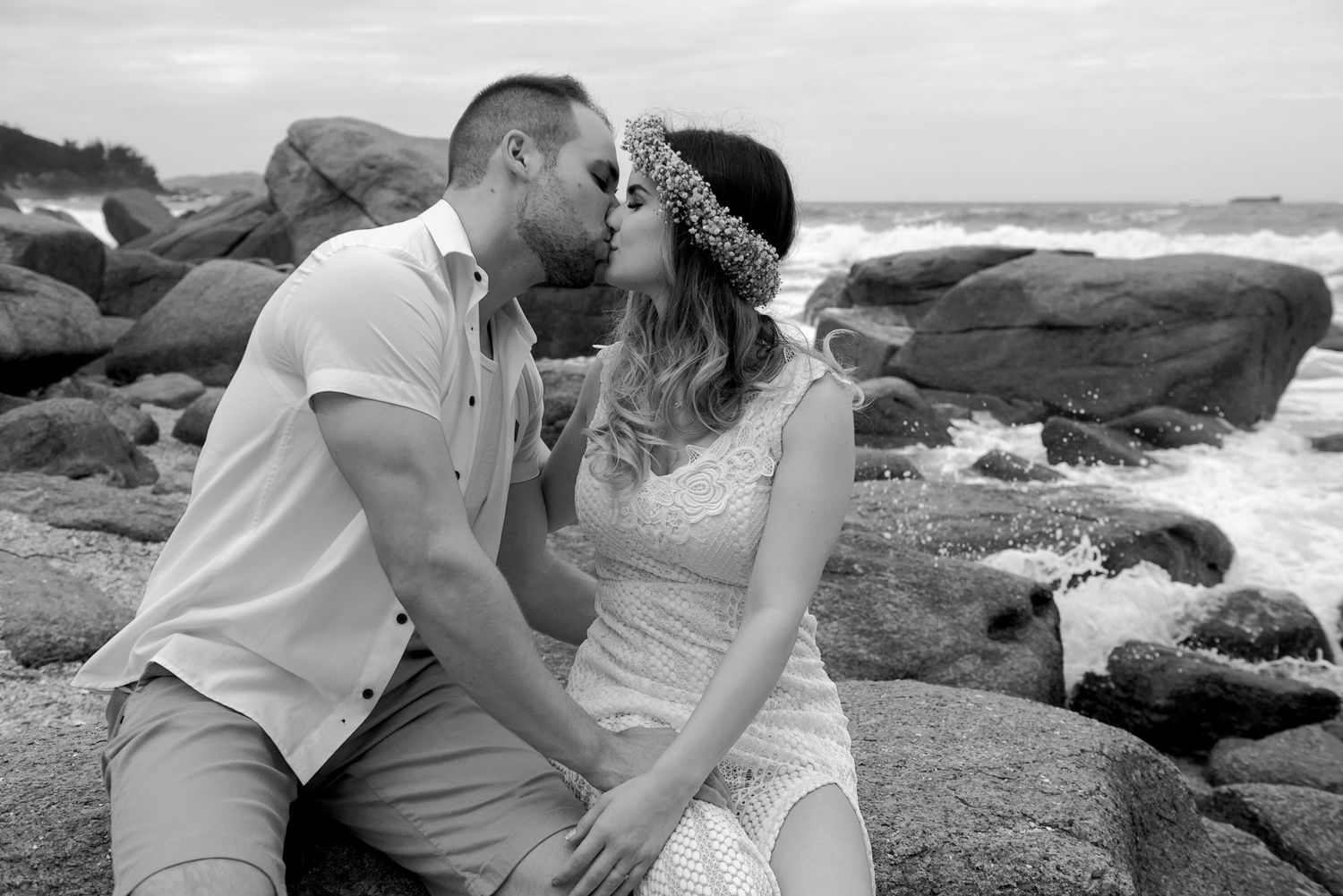 Couple shares tender moment on rocky coastal shore in black and white.