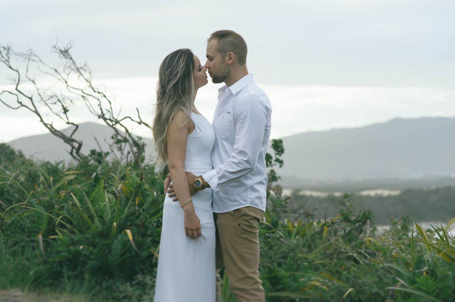 Intimate portrait of a couple against a mountainous coastal landscape at dusk.