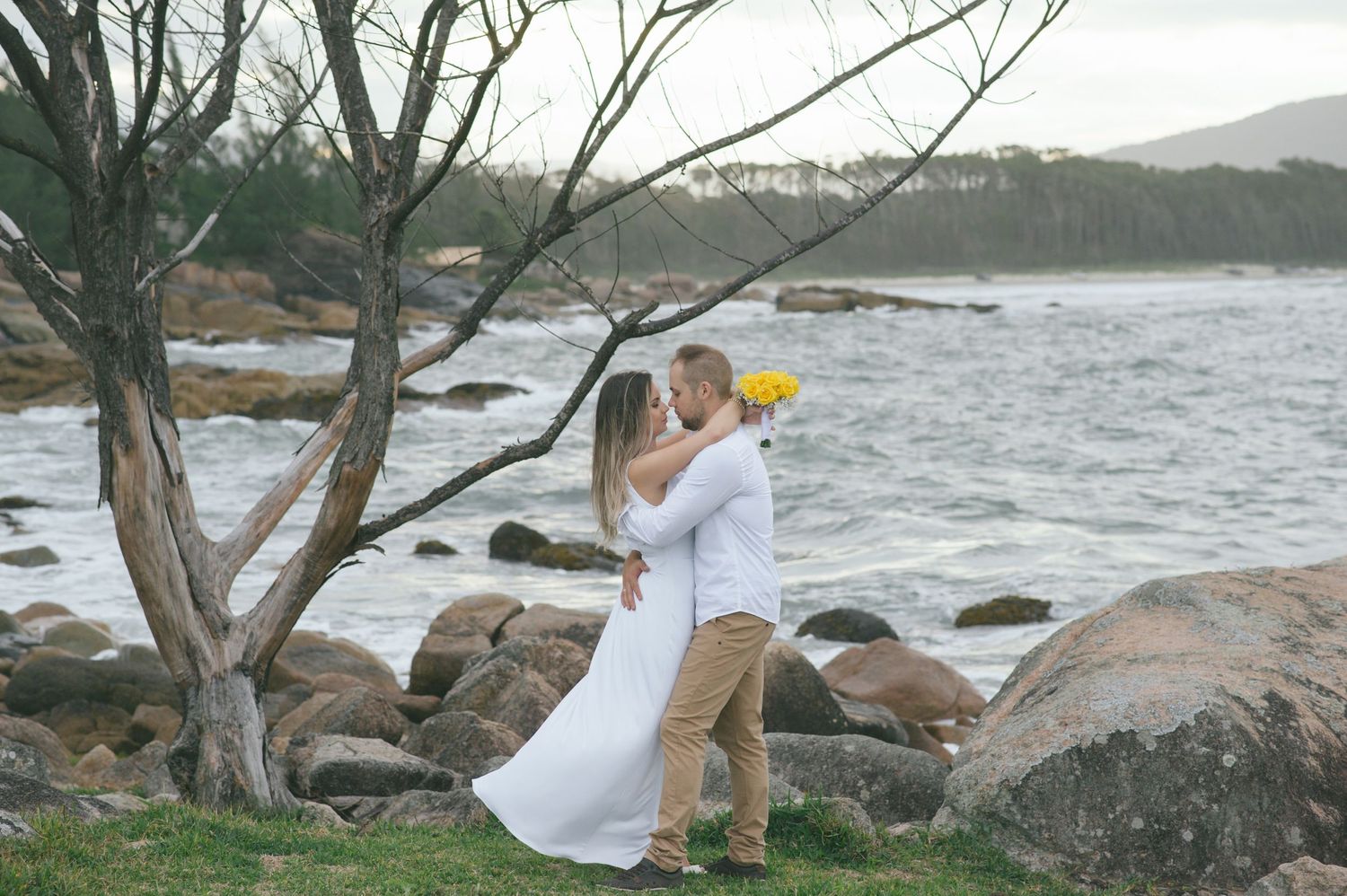 Romantic scene by the rocky coastline with bare trees and crashing waves in the background.
