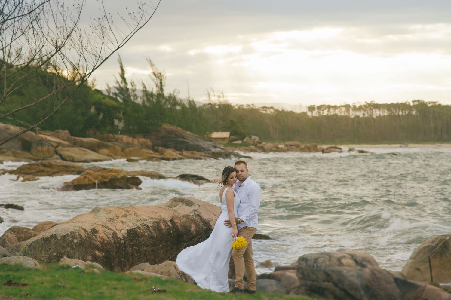 Sunset engagement photo on rocky coastal outcrop with waves crashing in the background.