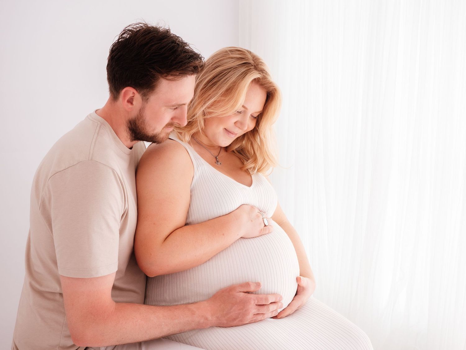 beautiful pregnant couple in cream pose looking at baby belly, taken by Verity Photography in Didcot