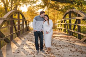 A couple walks hand in hand on a wooden bridge surrounded by golden autumn foliage at sunset.