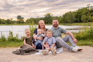 Family lounging together on pathway by scenic lake during golden hour sunset.
