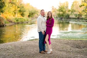 A couple shares a romantic moment by a scenic river during golden hour autumn photography session.
