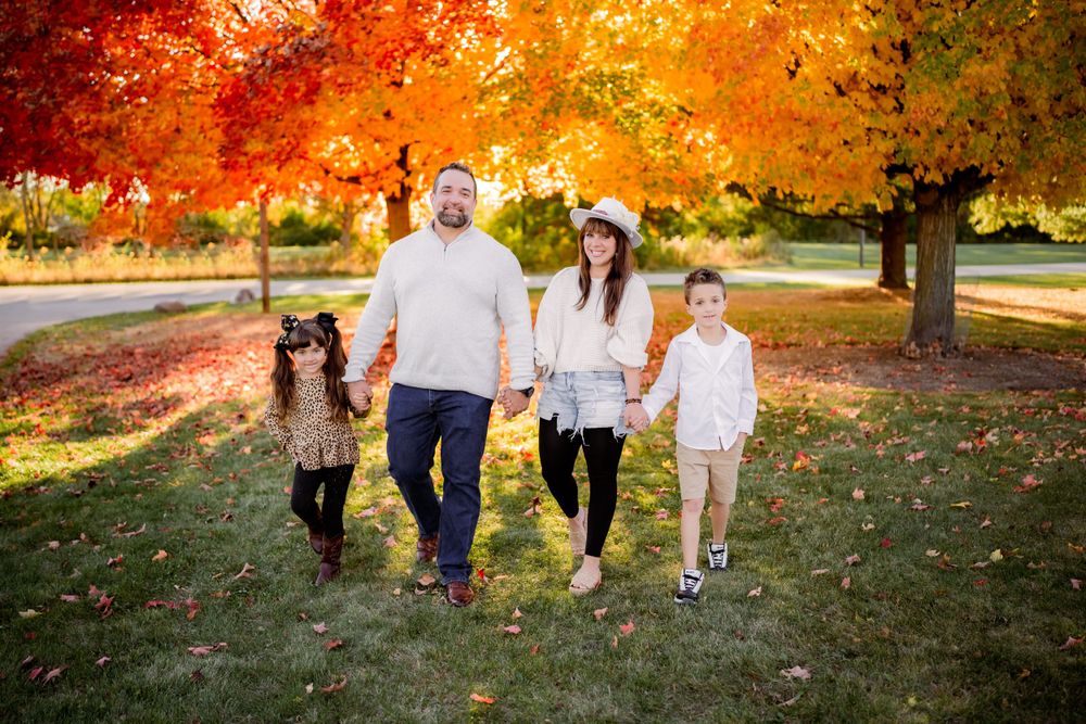 A family walks together on fallen autumn leaves under vibrant orange maple trees.