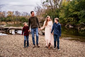 Family walking together along riverbank with autumn trees in background.