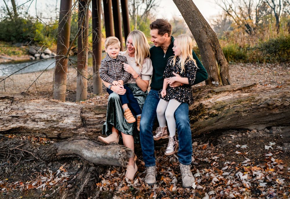 Family sitting together on fallen tree trunk by river during autumn.