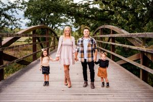 A family walks together holding hands on a wooden bridge surrounded by trees.