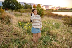 A person in casual clothing stands in a golden field during sunset with tall grass and trees in the background.