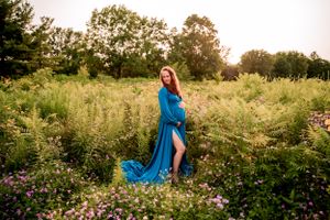 Woman in flowing blue dress stands in wildflower meadow at sunset.