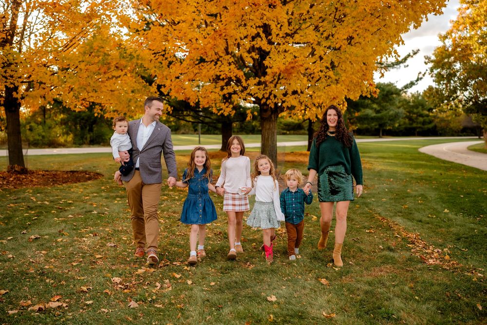 A group walks together through a scenic autumn park with golden leaves falling from trees in the background.
