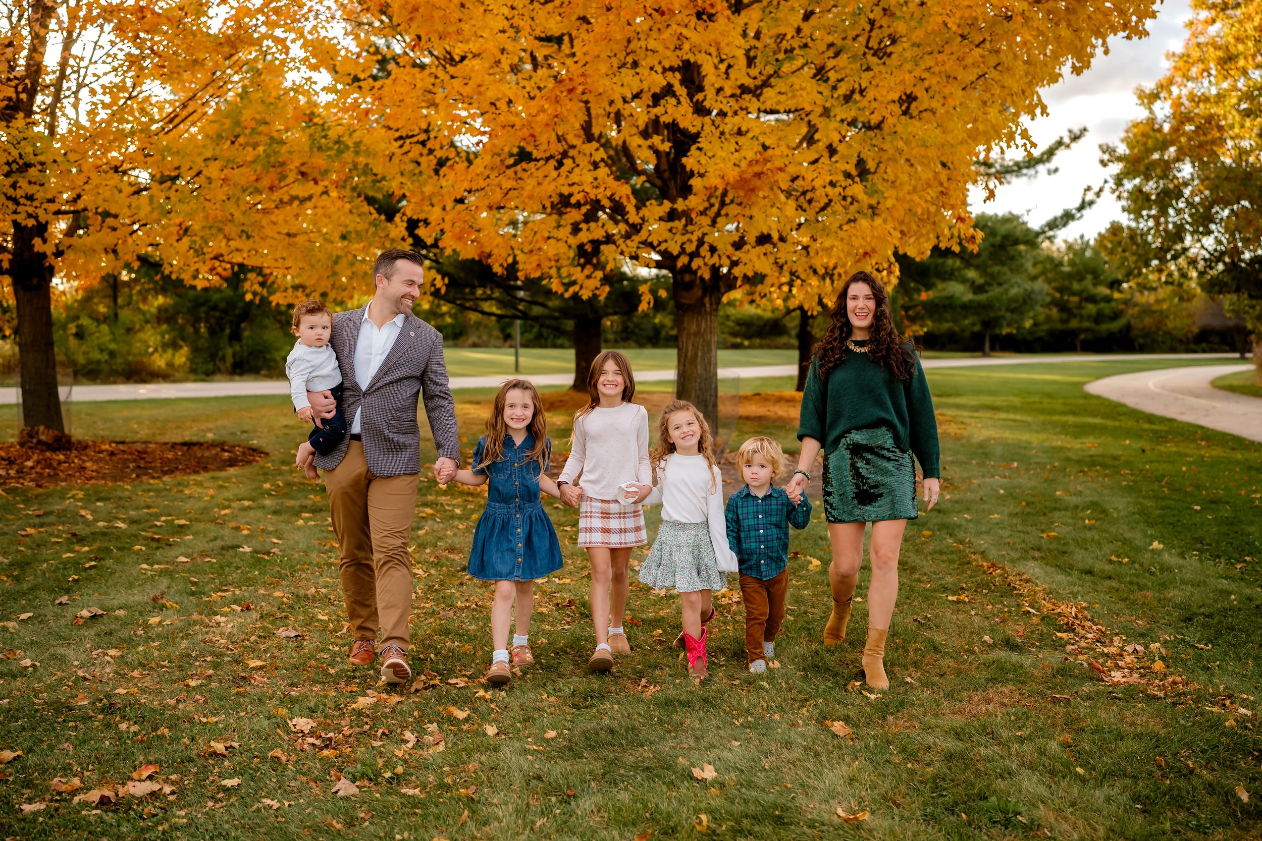 A group walks together through a scenic autumn park with golden leaves falling from trees in the background.