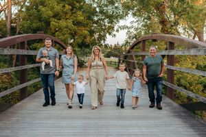 Group walking together and holding hands on a wooden bridge during golden hour at sunset.