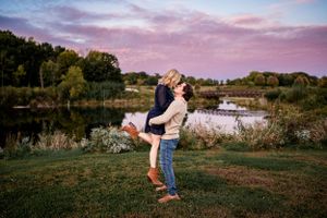 A romantic sunset embrace by a serene lake with pink clouds overhead.