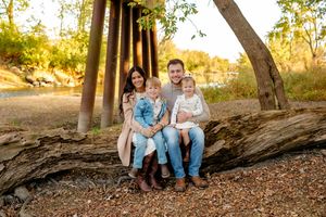 A couple sits together on a fallen tree trunk in a wooded area during golden hour lighting.