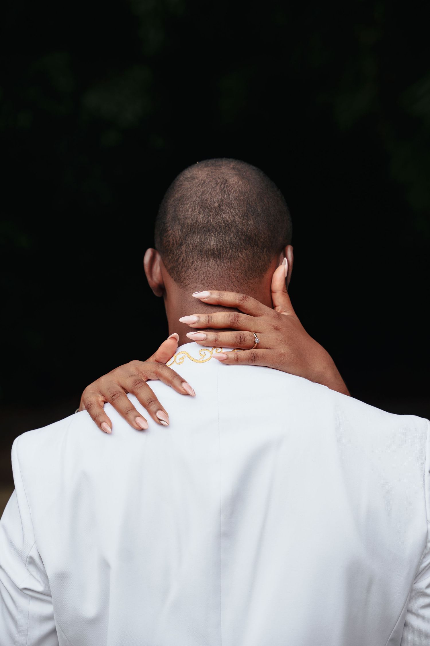 Back view of a person in white formal wear with hands embracing their neck.