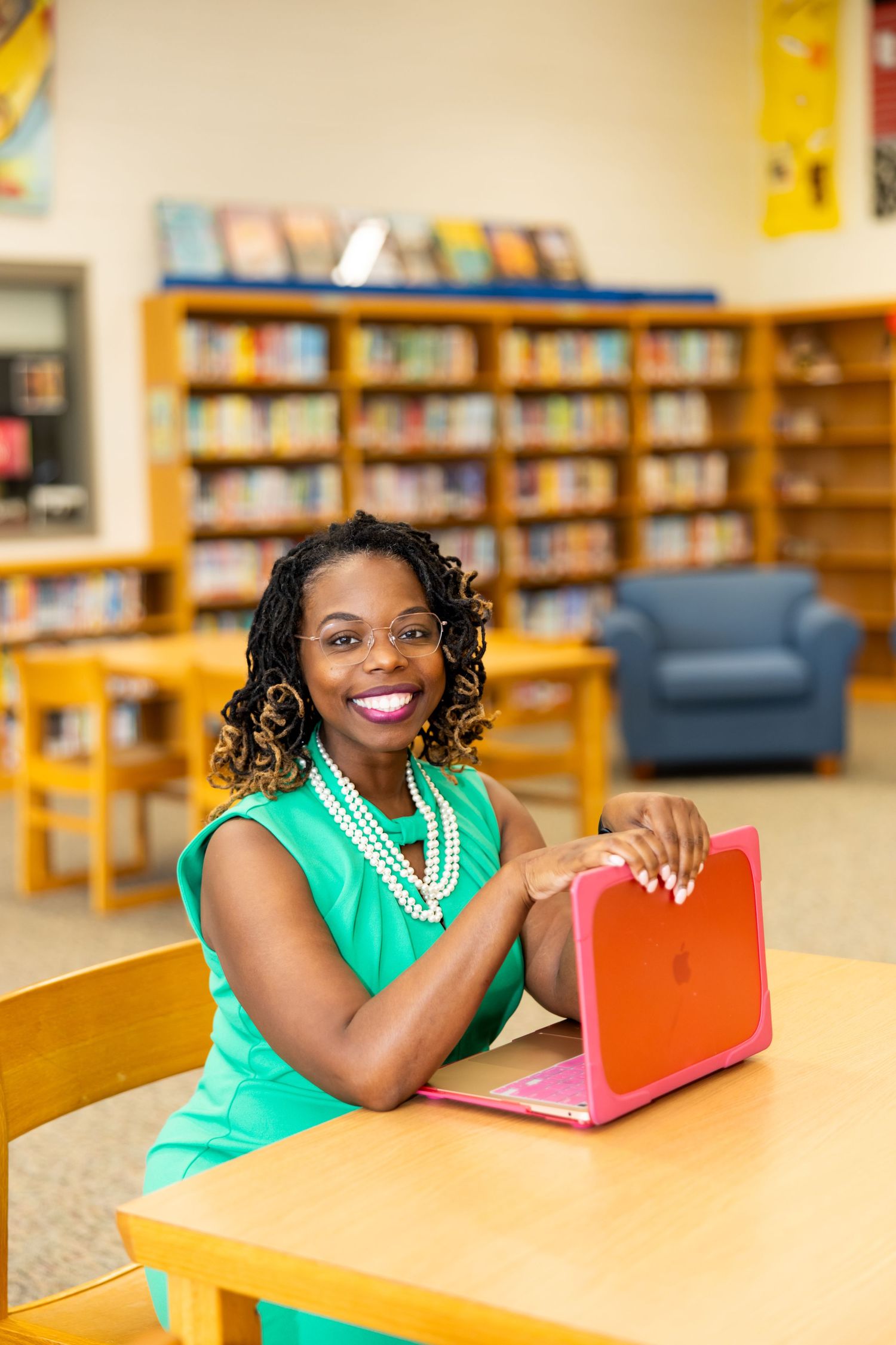Student in bright green top studies with colorful books at library table.