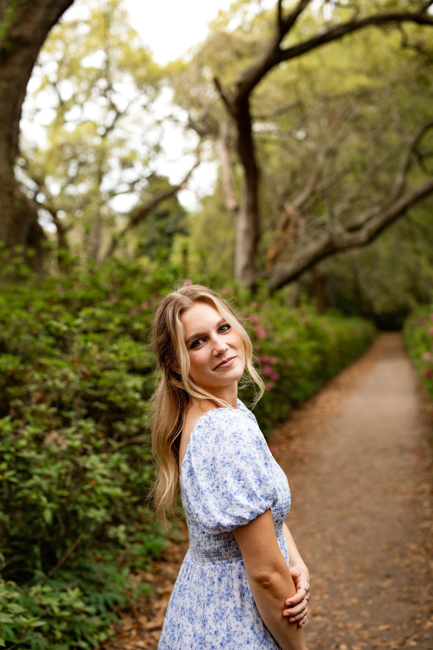 Someone wearing a blue and white floral dress poses on a scenic forest trail surrounded by lush greenery.