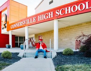 A person sits on steps outside the entrance of Connersville High School on a sunny day.