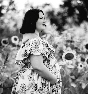 A person in a floral off-shoulder dress poses in a field of white flowers on a sunny day, creating a dreamy black and white scene.