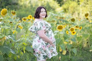 Person in a floral dress poses in a vibrant sunflower field during golden hour.