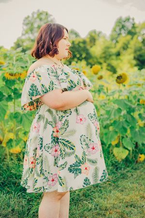 Floral tropical dress swaying in a sunlit sunflower field with lush greenery in the background.