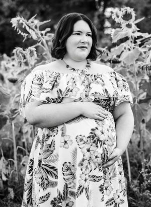 Black and white portrait of someone in a floral dress standing in front of sunflowers, with natural lighting outdoors.