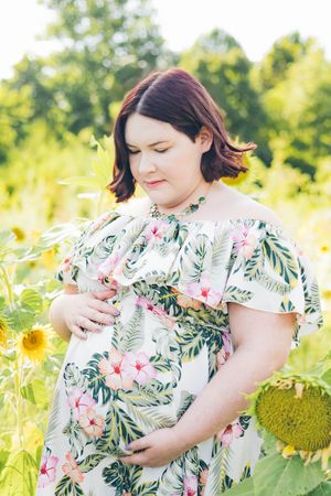 A person in a floral dress stands amid blooming sunflowers in a sunlit field on a warm summer day.