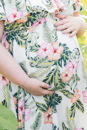 A close-up of hands resting on a floral dress with tropical leaves and pink hibiscus print against a light background.