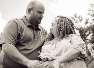 A couple shares a tender moment together outdoors in black and white as they smile at each other.