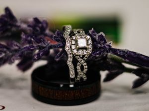 Sparkling diamond engagement ring set against purple lavender stems and a dark band base in soft focus.
