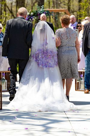 Wedding processional with bride in white gown with purple accents walking outdoors on sunny day.