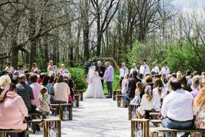 Wedding ceremony taking place outdoors on a wooden boardwalk path surrounded by trees and guests seated on benches.