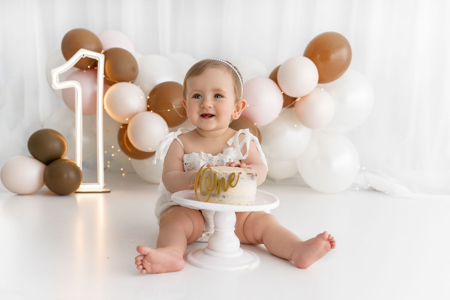 Baby's first birthday cake smash setup with brown and white balloon decorations.