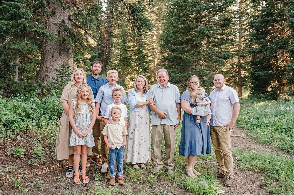 Extended family gathering poses for portraits among tall evergreen trees.