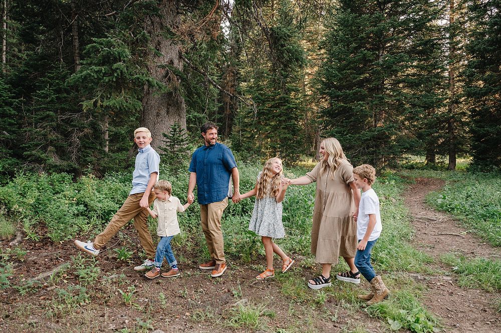 Family holding hands and walking together on a forest path surrounded by evergreen trees.