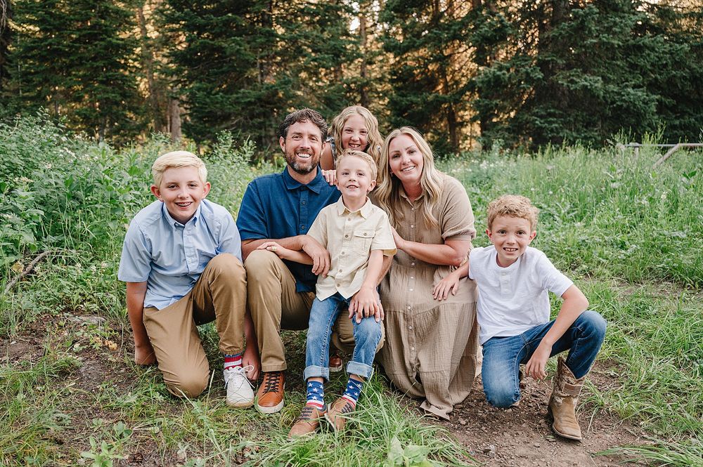 Casual family portrait taken outdoors with forest greenery and trees in background.