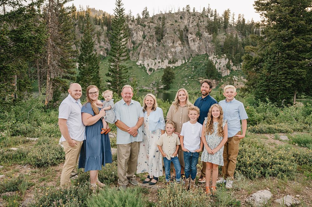 Extended family gathered for group photo with mountain cliffs and evergreen forest in background.